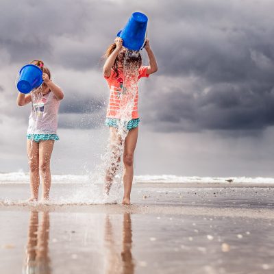 Two little girls dump buckets of water on their heads.