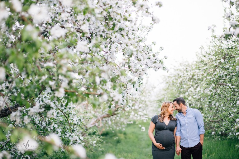 maternity portrait of man and woman standing near rows of blooming trees by Sonia Bourdon