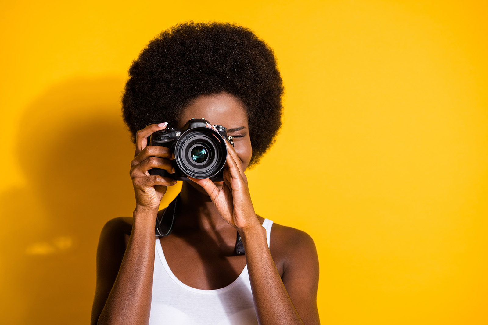 Black woman with camera up to eye on yellow background