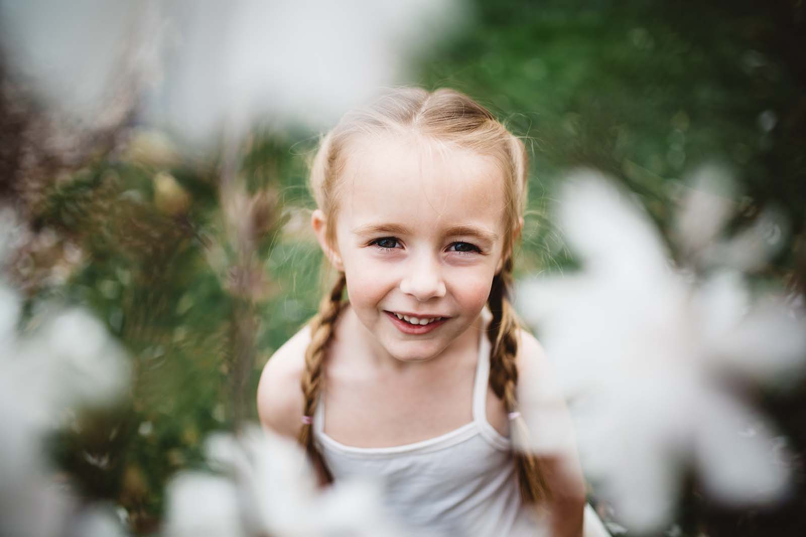 A smiling girl through flowers. Finding balance with photography and motherhood