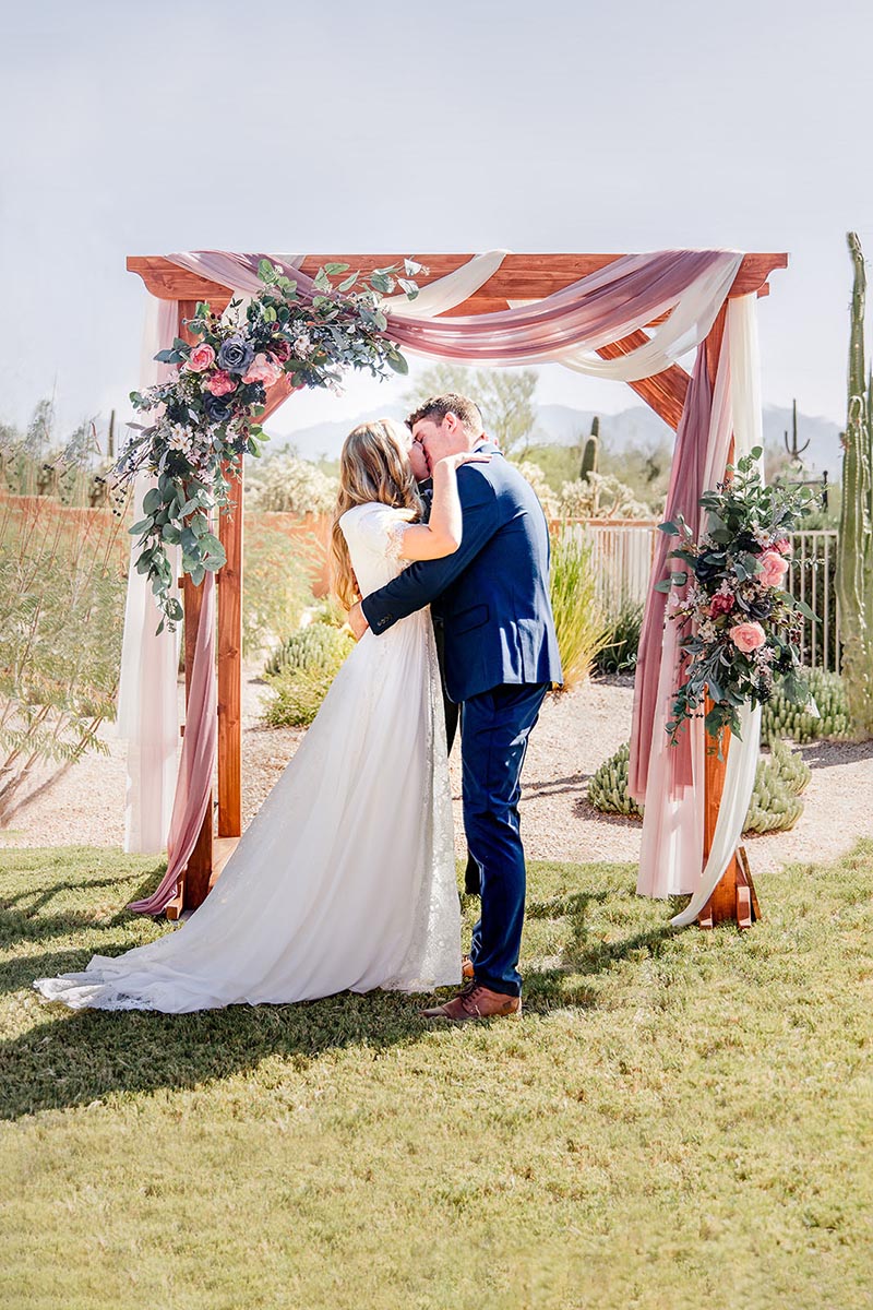 Rachael Wardell @Rachael_Elizabeth_Wardelll love in the time of covid Couple stands under arch during Covid beach wedding