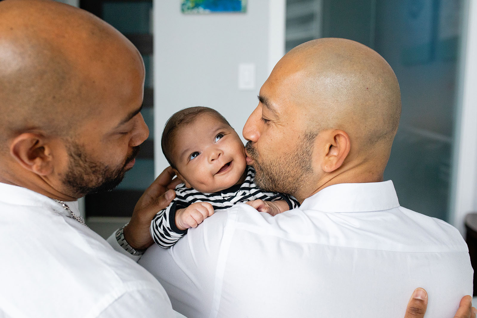 Dads kiss their baby during newborn photo session