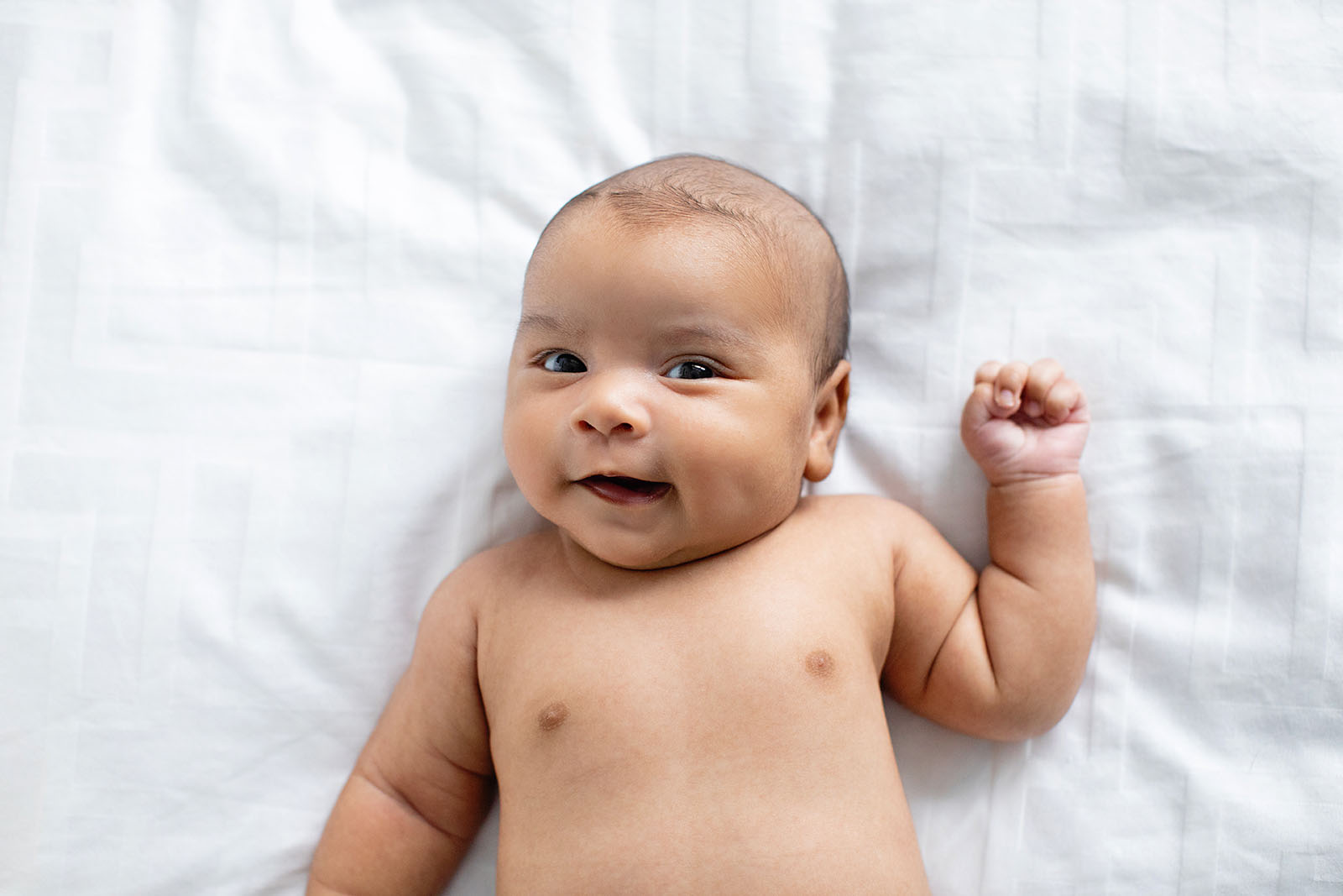 Smiling newborn baby on white sheet